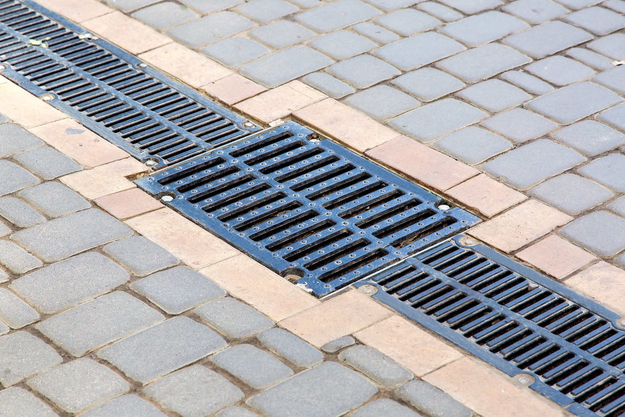 A lattice of a drainage paving system with hatch grill on a path made of square stone tiles, close up of a rainwater drainage system.